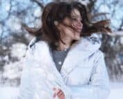 Femme avec un manteau blanc en hiver, les cheveux au vent