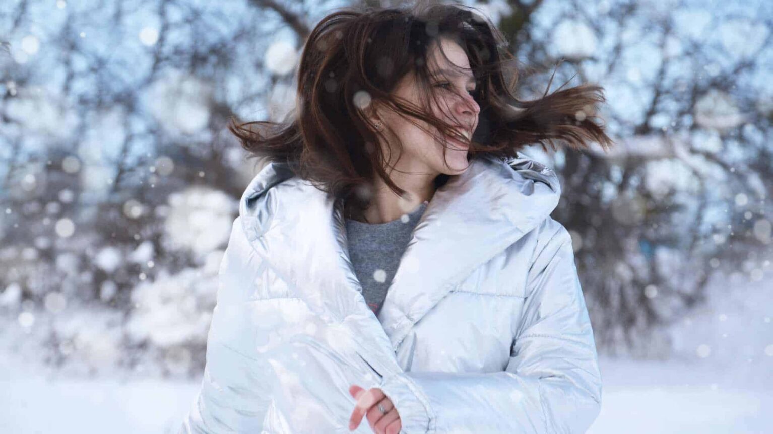 Femme avec un manteau blanc en hiver, les cheveux au vent