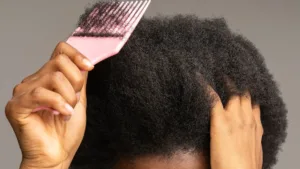 Une personne utilise un peigne afro pour coiffer ses cheveux, une étape clé de la routine capillaire pour cheveux crépus.