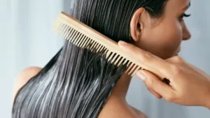 Gros plan sur une femme démêlant ses cheveux mouillés et traités avec un peigne en bois, potentiellement pour la porosité des cheveux.