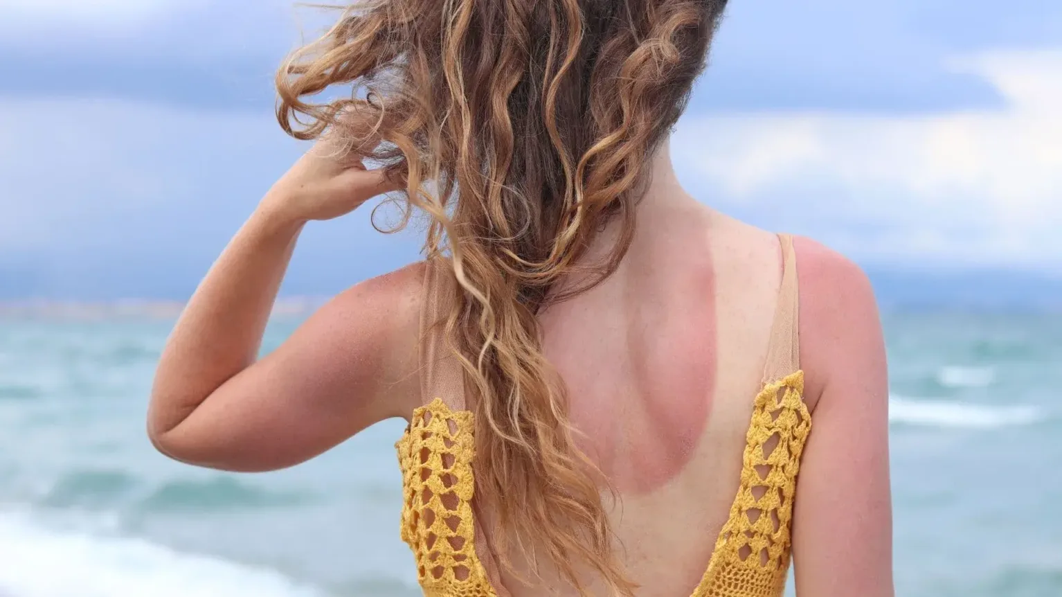Une femme blonde tient ses cheveux abimés et secs au soleil.