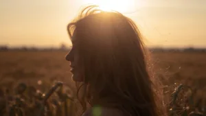 femme sous le soleil dans un champs les cheveux au vent